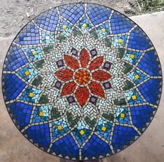 a round glass table with a flower design on it's top, sitting on the ground