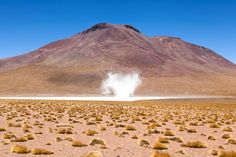 a large mountain in the distance with some dust coming out of it's top