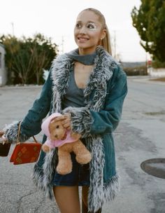 a woman is holding a teddy bear in her hand while walking down the street,