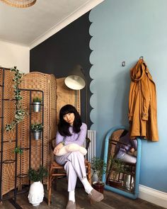 a woman sitting on a chair in front of a wall with plants and other items