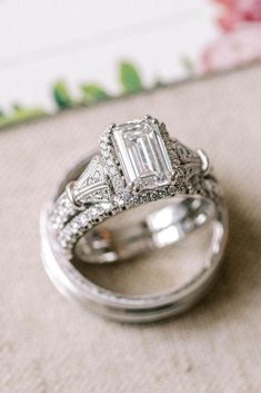 two wedding rings sitting on top of each other next to a flowered cloth covered table