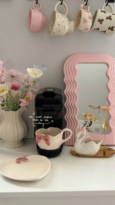 a white table topped with plates and cups filled with flowers next to a pink mirror