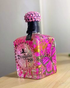 a pink and gold perfume bottle sitting on top of a wooden table