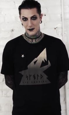 a man with black makeup and piercings standing in front of a white brick wall