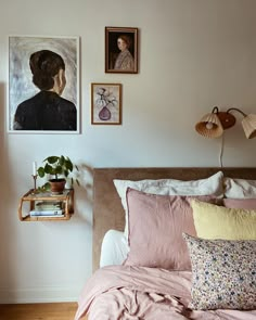 a bed with pink sheets and pillows in a bedroom next to pictures on the wall