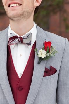 a man wearing a gray suit with a red bow tie and boutonniere