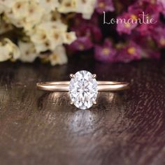 a white diamond ring sitting on top of a wooden table next to purple and white flowers