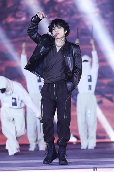 a male in a black leather jacket and pants on stage with his hand up to his ear