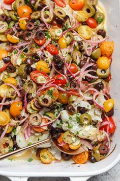 a white casserole dish filled with olives, onions, tomatoes and other vegetables