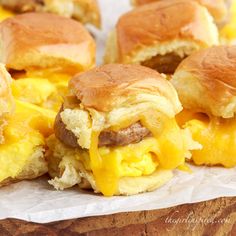 two breakfast sandwiches with cheese and meat on them sitting on wax paper next to some bread