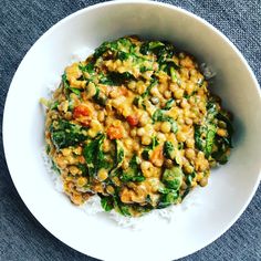 a white bowl filled with rice and vegetables on top of a blue table cloth next to a fork