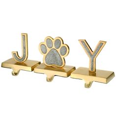 three gold metal letters with a dog's paw and the word joy on them