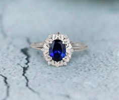 an oval shaped blue sapphire and diamond ring on top of a white surface with cracks in the background