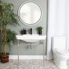 a white sink sitting under a round mirror next to a potted bamboo plant in a bathroom