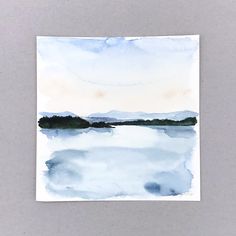 a watercolor painting of a lake with mountains in the distance and blue sky above