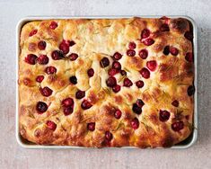 a baked pastry with cherries and rosemary in a metal pan on a table top