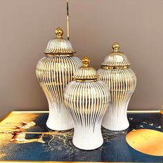 three white vases sitting on top of a table next to each other with gold accents