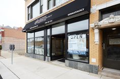 an empty sidewalk in front of a building with signs on the windows that say open