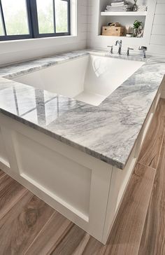 a large white sink sitting under a window next to a wooden counter top in a bathroom