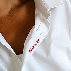 a woman wearing a white shirt with red writing on the chest and collar is smiling at the camera