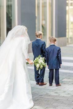 the bride and groom are walking down the street with their little boys dressed in blue