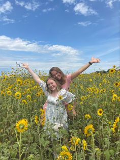 two girls are standing in a field full of sunflowers and one is holding her arms up