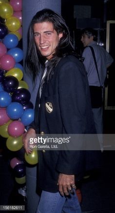 an image of a man with long hair and balloons in the background at an event