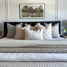 a bed with many pillows on top of it and a painting above the headboard