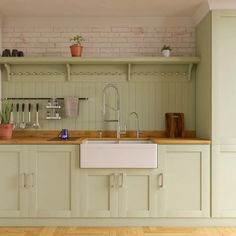 a kitchen with green cabinets and white walls, wood flooring and an open shelving unit above the sink