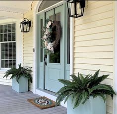 a front porch with two planters and a wreath on the door sill next to it