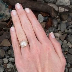 a woman's hand with a pearl ring on top of her finger and rocks in the background