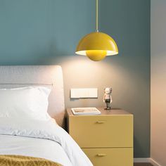 a yellow lamp hanging over a bed next to a night stand