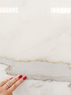 a woman's hand with red nail polish holding onto the edge of a marble slab