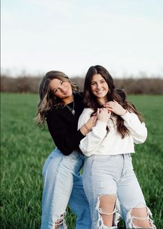 two young women are posing for a photo in the middle of a grassy field with their arms around each other