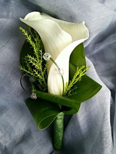 a white calla lily and greenery boutonniere on a blue cloth