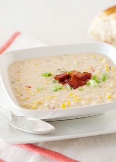 a bowl of soup with bacon and green onions in it on a white plate next to a piece of bread