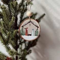 a christmas ornament hanging from the top of a pine tree with a nativity scene on it