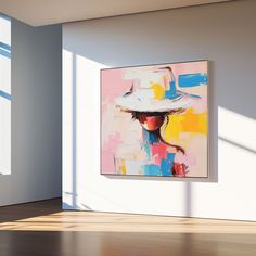 an abstract painting hangs in the corner of a white room with sunlight streaming through it