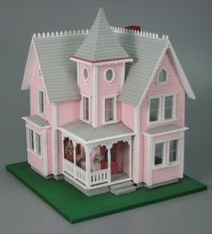 a pink doll house with white trim on the front and side windows, sitting on a green mat