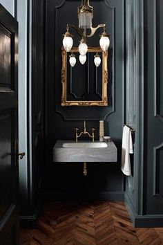 an image of a bathroom with black walls and gold accents on the mirror above the sink