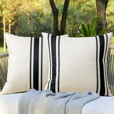 two black and white pillows sitting on top of a couch next to a tree in the background