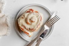 a plate with a cinnamon roll on it next to a fork and napkin, along with silverware