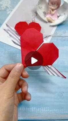 someone is holding up some paper hearts on a blue table with an angel in the background