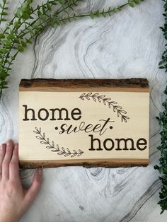 a hand holding a wooden sign that says home sweet home with leaves around the edge