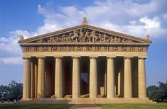 an old building with columns and statues on the front, against a blue cloudy sky