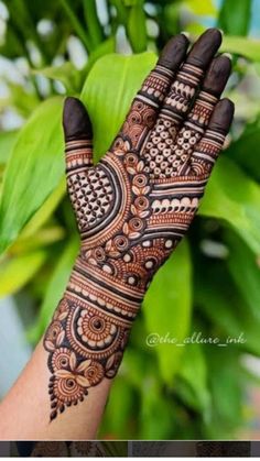 a woman's hand with henna tattoos on it and green leaves in the background