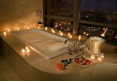 a bathtub with candles and flowers on the counter in front of a large window