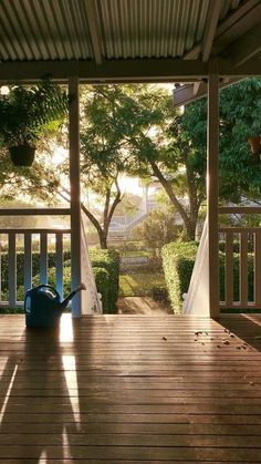 a blue watering can sitting on top of a wooden deck next to a tree and bushes