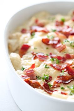 a white bowl filled with cheese and bacon on top of a table next to a fork