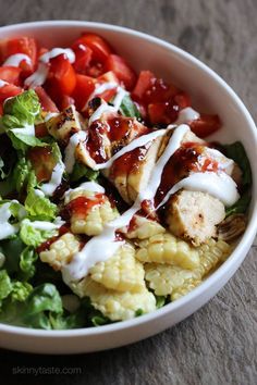 a white bowl filled with salad and chicken covered in ranch dressing on top of cauliflower